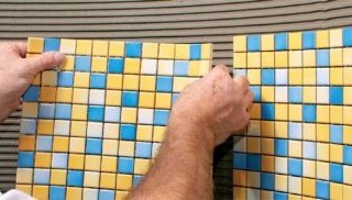 Процесс приклеивания плитки мозаики на стену в ванной